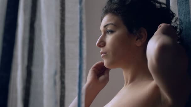 Pensive, young brunette touching her hair at the window — Stock Video