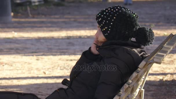 Vrolijke vrouw op houten bankje in het park tijdens het gesprek op de telefoon — Stockvideo