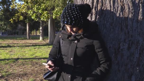 Femme appuyée contre un arbre envoie un message avec smartphone — Video