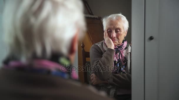 Sad and depressed old woman in the mirror touches face — Stock Video