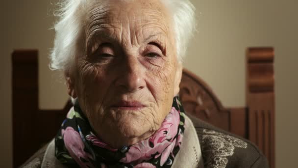 Стара бабуся сидить, дивлячись на камеру і закриває очі — стокове відео
