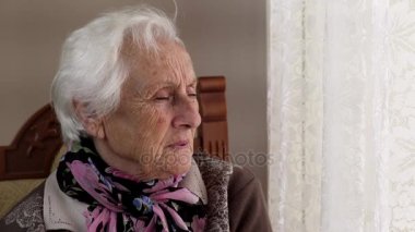 yaşlı, üzgün kadın ikindilerde pencereden görünüyor