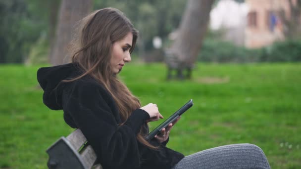 Το προφίλ του πορτρέτο του όμορφη γυναίκα κοιτάζοντας βιαστικά τον υπολογιστή tablet στο πάρκο — Αρχείο Βίντεο