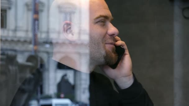 Perfil del hombre calvo sonriendo hablando por teléfono, detrás de una ventana de cristal — Vídeo de stock