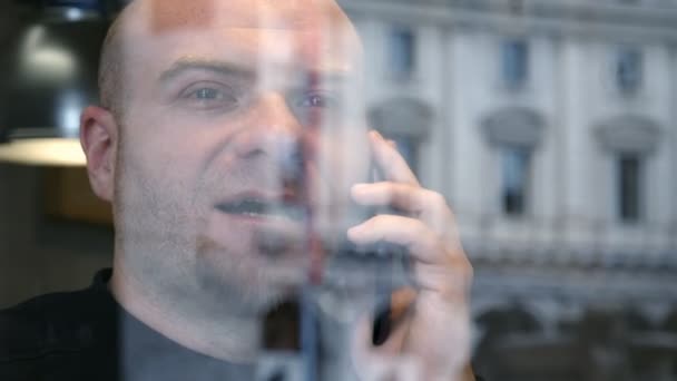 Primer plano en el hombre calvo hablando por teléfono detrás del cristal de la ventana — Vídeo de stock