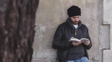 Genç adam okuyan, konsantre bir duvara yaslanmış