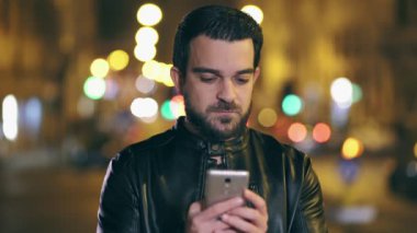 Gülümseyen latin adam bir sms ile smartphone, şehir ışıkları, gece arka plan gönderir.