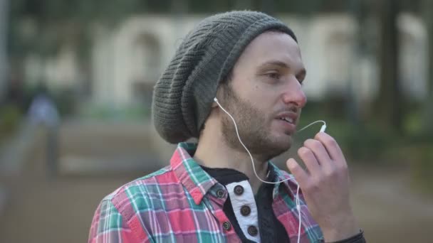 Sonriente guapo en el parque hablando por teléfono con los auriculares — Vídeos de Stock
