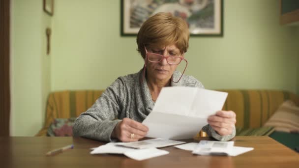 Mujer madura con gafas rojas se ve preocupada por las facturas a pagar — Vídeo de stock