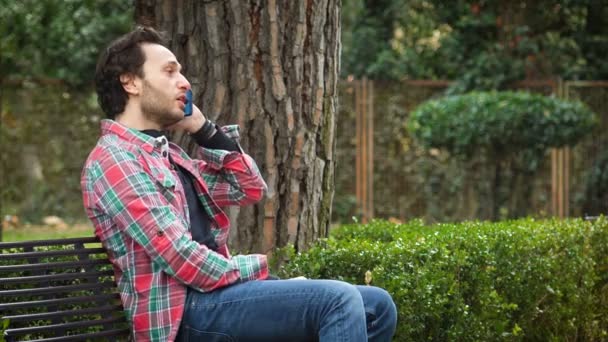 Portrait of Nervous handsome man talking on the phone with earphone at the park — Stock Video