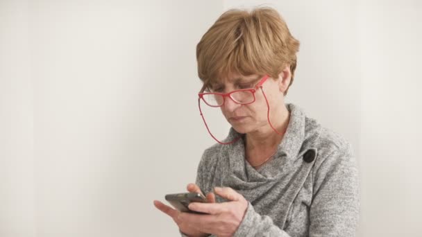 Portret van rijpe blonde vrouw met een rode bril te typen op de smartphone — Stockvideo
