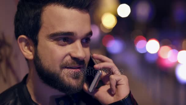 Vicino al giovane uomo allegro che parla al telefono di notte, in città — Video Stock