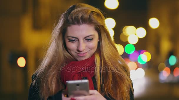 Gülümseyen genç sarışın kız smartphone üzerinde yazarak şehir gece — Stok video