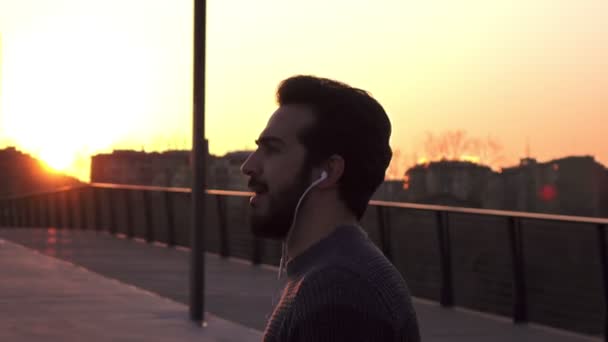 Gelukkig jongeman die dansen luisteren naar muziek voor de stad bij zonsondergang — Stockvideo