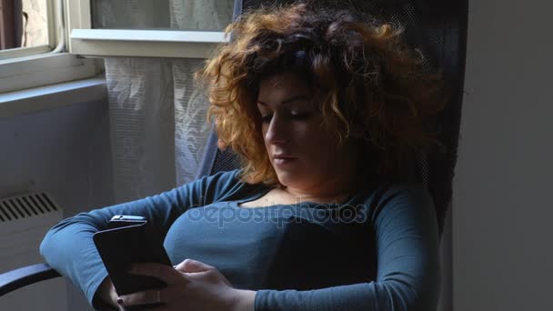 スマート フォンを使用している間は家で座っている若い女性 — ストック動画