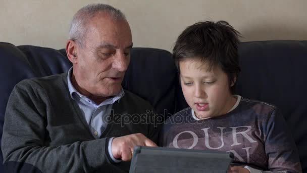 祖父が孫のタブレットを使用してソファの上に教えています。 — ストック動画