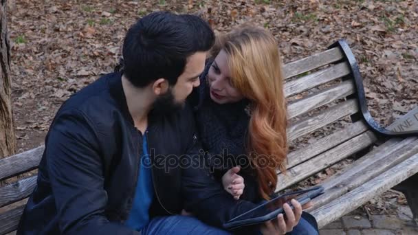 Heureux couple romantique avec tablette informatique, relaxant sur le banc du parc — Video