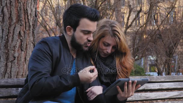 Couple détendu sur un banc au parc jouer avec la tablette — Video