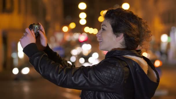 Smiling brunette shoots funny selfie, city nights in the background — Stock Video