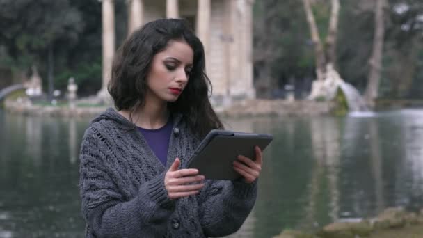 Belle jeune femme près du lac tout en utilisant la tablette — Video