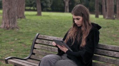 Güzel kadın parkta bir bankta oturmuş tablet kullanır