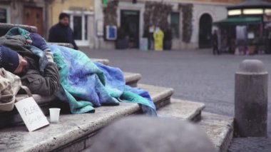 focus on  homeless man sleeps on the stairs of a fountain, while a man give him money
