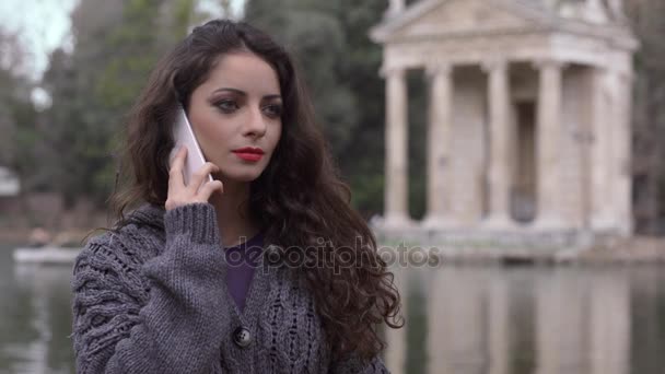 Retrato de Sorrindo morena no parque falando no telefone, lago no fundo — Vídeo de Stock