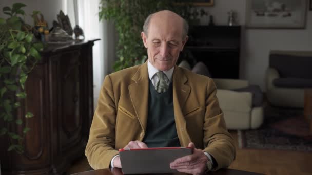 Sonriendo elegante hombre mayor utilizando tableta de ordenador en casa . — Vídeos de Stock