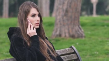 Genç güzel kadın telefonla konuşuyor bankta