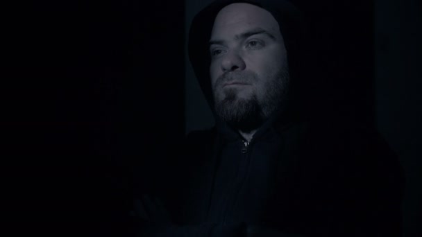 Закрыть глаза на грустного и обаятельного человека с капюшоном в темноте — стоковое видео