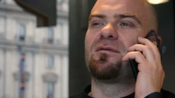 Primer plano en el hombre calvo hablando por teléfono detrás del cristal de la ventana — Vídeos de Stock