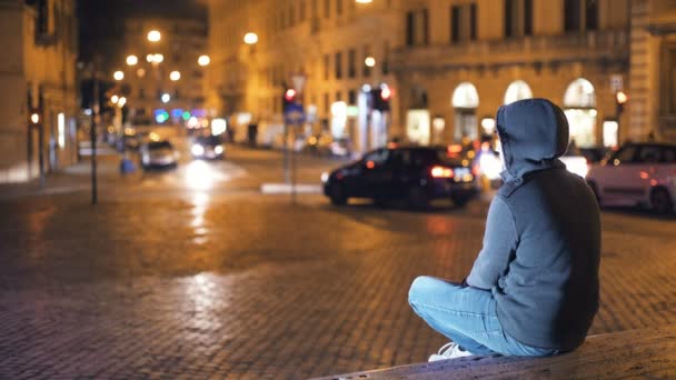 Joven con capucha contempla la ciudad por la noche — Vídeo de stock