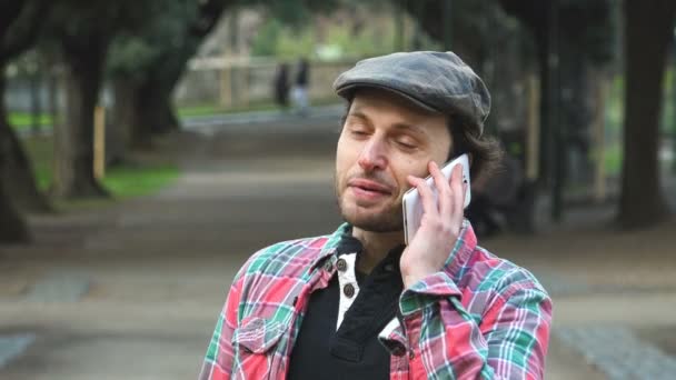 Улыбающийся мужчина в парке разговаривает по телефону — стоковое видео