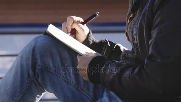 Закройте на руке человека, пишущего дневник под деревом — стоковое видео