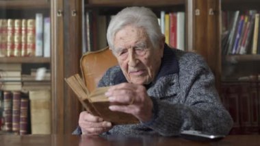 Çok yaşlı adam masada oturan bir kitap okuma portresi