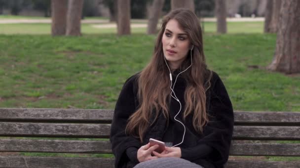 Горгеус молодая женщина сидит на скамейке и слушает музыку, поет — стоковое видео