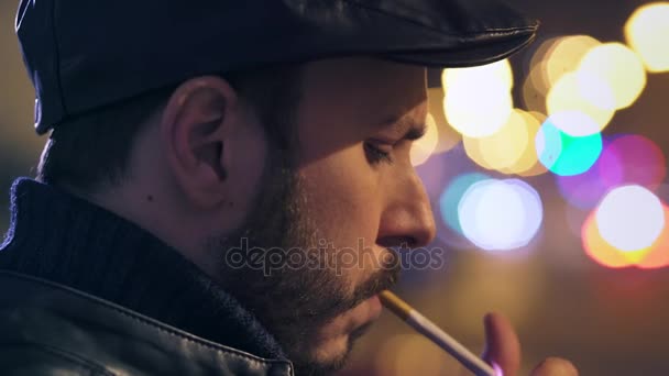 Un homme seul et réfléchi allume une cigarette la nuit en ville, gros plan — Video