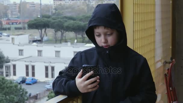 Jonge jongen op het balkon tijdens het gesprek op de telefoon met zijn ouders — Stockvideo