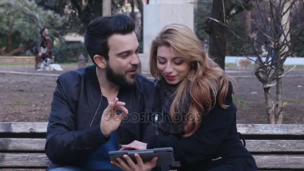 Portrait de couple heureux sur le banc en regardant des photos sur la tablette — Video