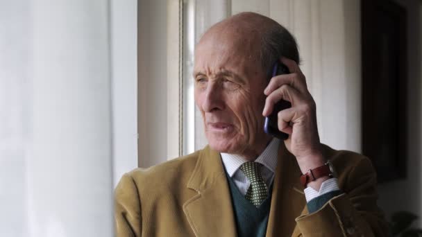 Uśmiechający się zadowolony starszy mężczyzna rozmawia przez telefon, opierając się w oknie — Wideo stockowe