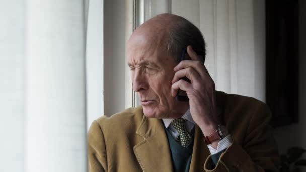 Портрет старого бізнесмена, який розмовляє по телефону у вікні — стокове відео