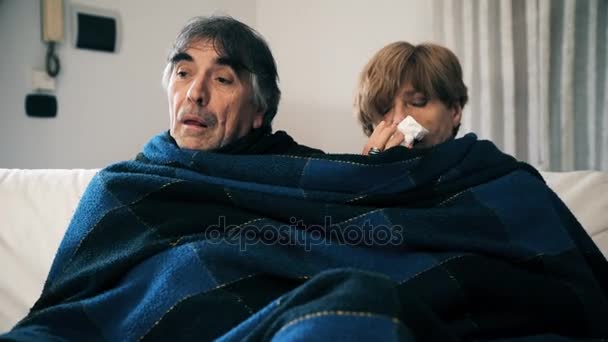 Зрелая пара с гриппом, сидящая под одеялами на диване — стоковое видео