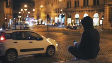 Yalnız basamaklarında oturan kişi smartphone şehirde geceleri kullanır