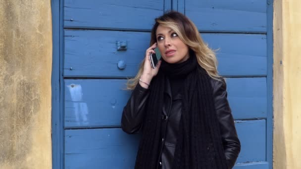 Loira mulher sexy falando no telefone inclinando-se no portão azul — Vídeo de Stock