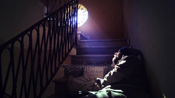Obdachloser, der in der Dämmerung auf der Treppe liegt, blickt auf das Licht, das aus dem Fenster kommt — Stockvideo