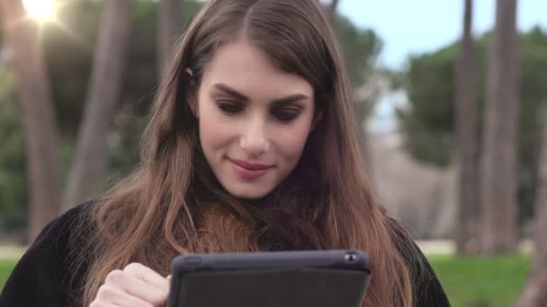 Привлекательная молодая девушка сосредоточилась на использовании планшета в парке — стоковое видео
