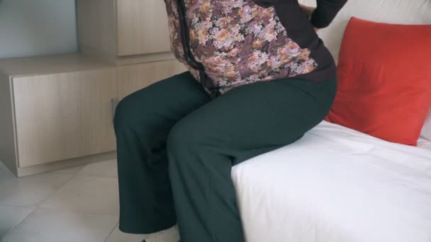 Літня жінка з артритом намагається встати з дивана — стокове відео