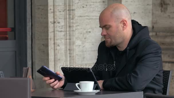 Homem careca sentado no bar enquanto usa smartphone e tablet — Vídeo de Stock