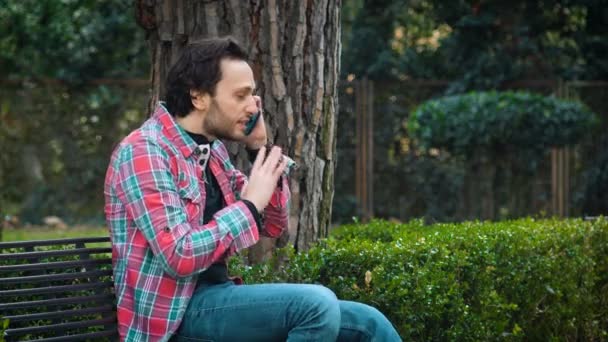 Profile of young nervous man on bench talking on the phone — Stock Video