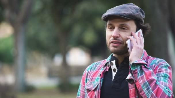 Улыбающийся и очаровательный мужчина в парке разговаривает по телефону — стоковое видео